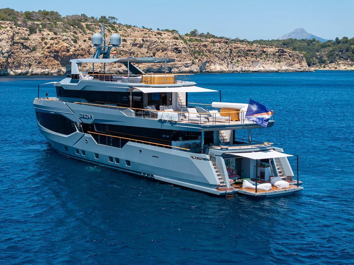 A luxurious yacht is anchored in clear blue waters with scenic cliffs in the background. aboard OSCAR Yacht for Sale