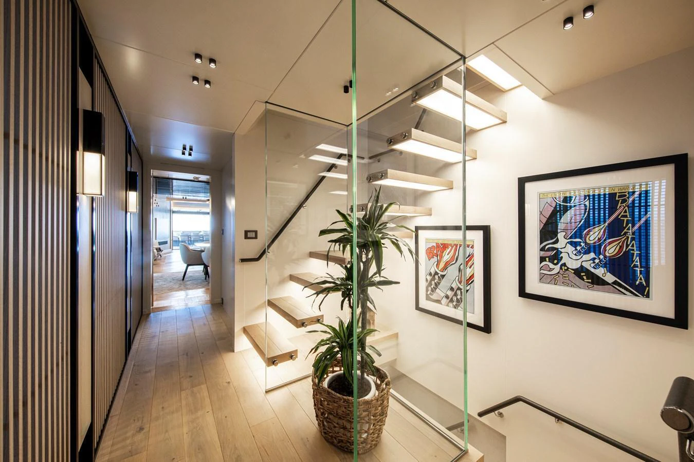 A stylish interior hallway featuring a modern staircase with glass railings and contemporary artwork. aboard OSCAR Yacht for Sale