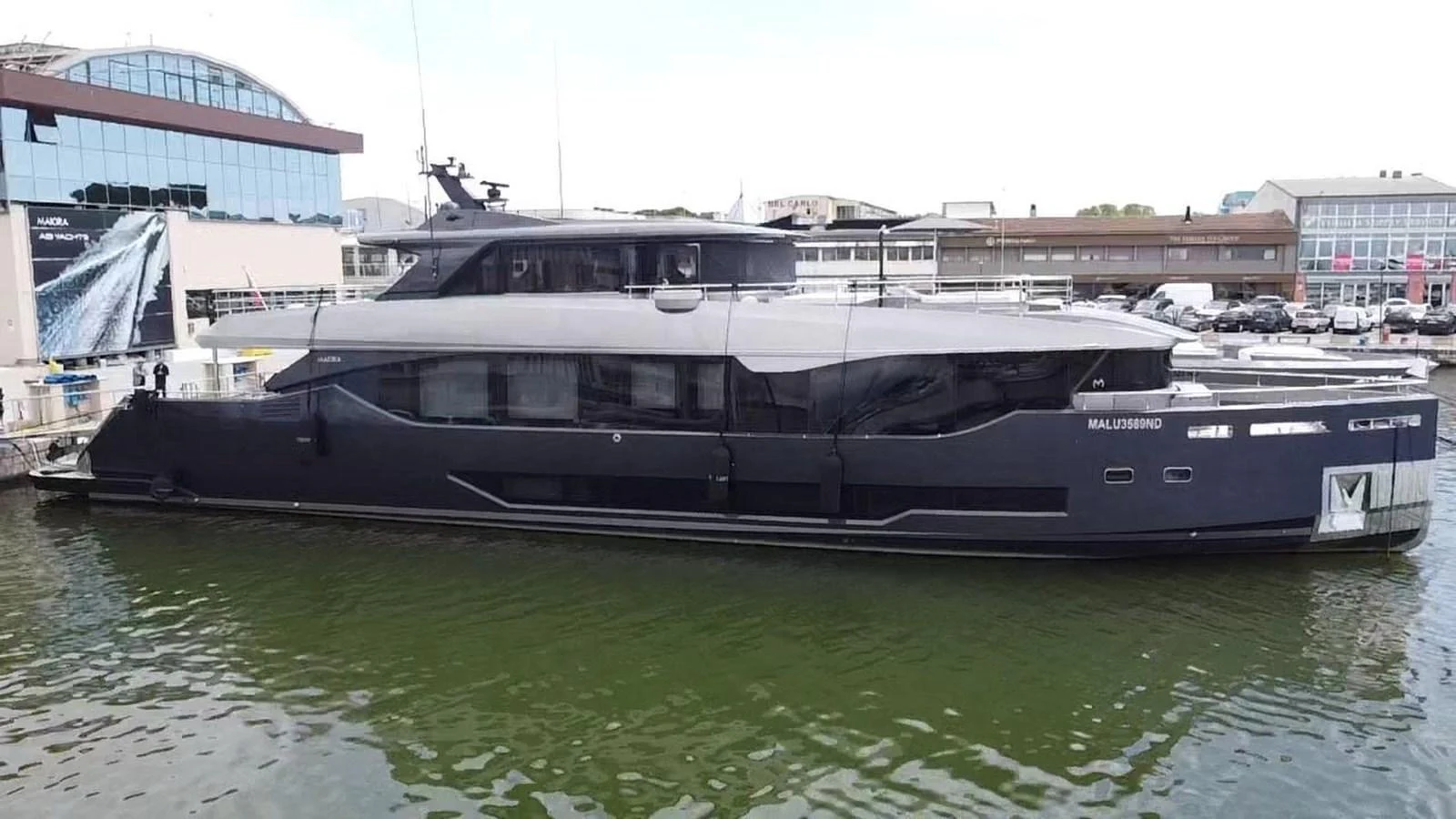 A sleek, modern yacht is docked at a marina, showcasing its stylish design and dark hull. aboard LADY BETTY Yacht for Sale