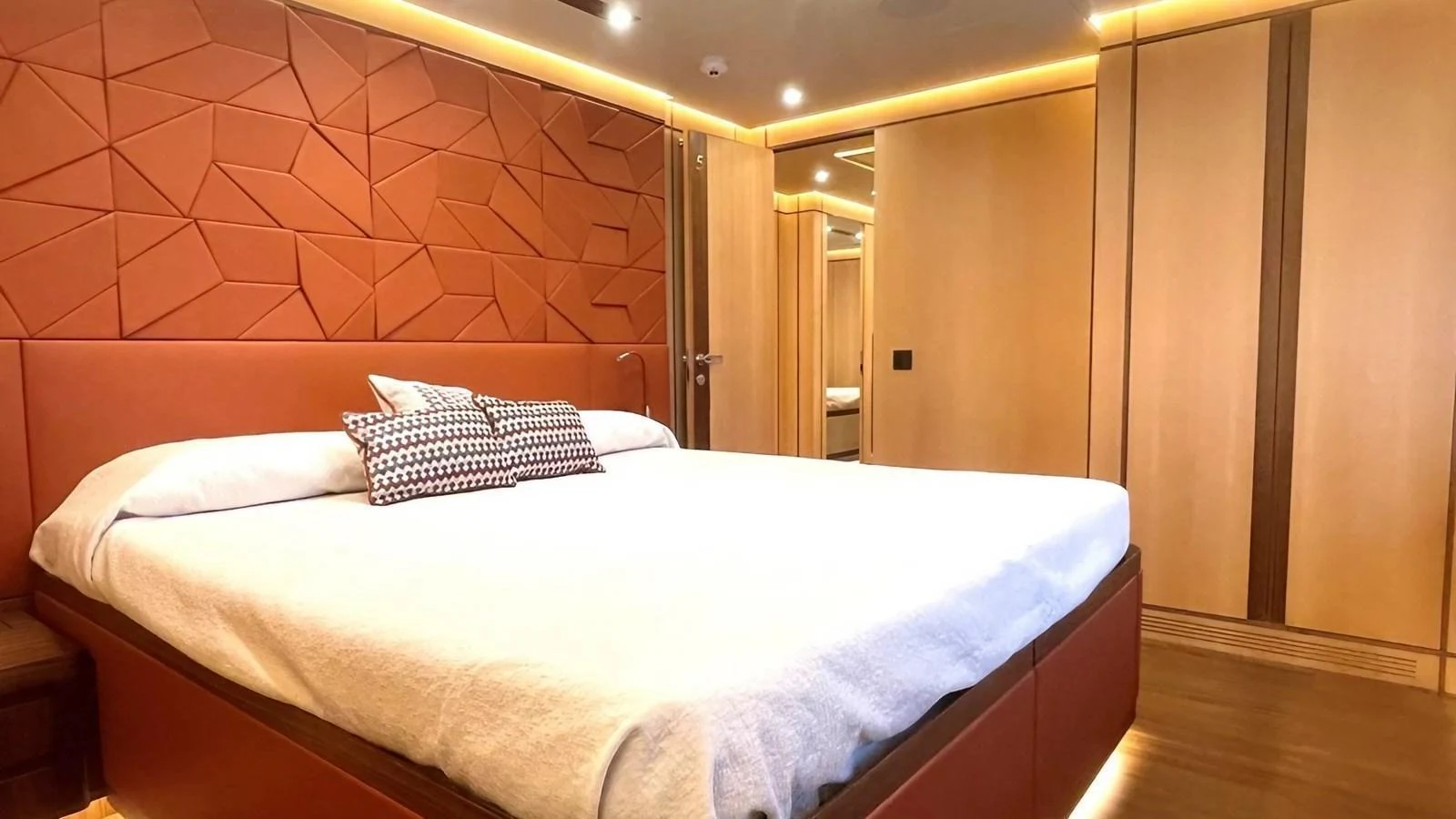 The stateroom features a luxurious bed with modern geometric wall design and warm lighting. aboard LADY BETTY Yacht for Sale