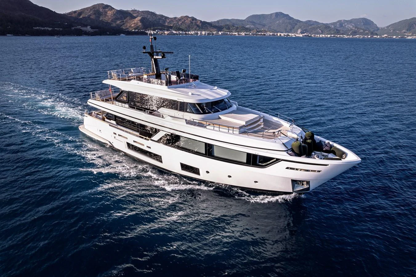 A sleek and modern yacht cruising on calm blue waters with a scenic mountainous backdrop. aboard BELLE ILE Yacht for Sale