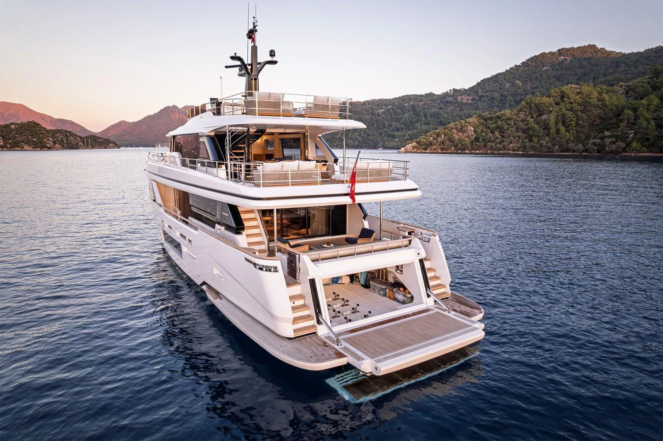 A luxurious yacht anchored in a serene bay with a spacious aft deck and inviting swim platform. aboard BELLE ILE Yacht for Sale