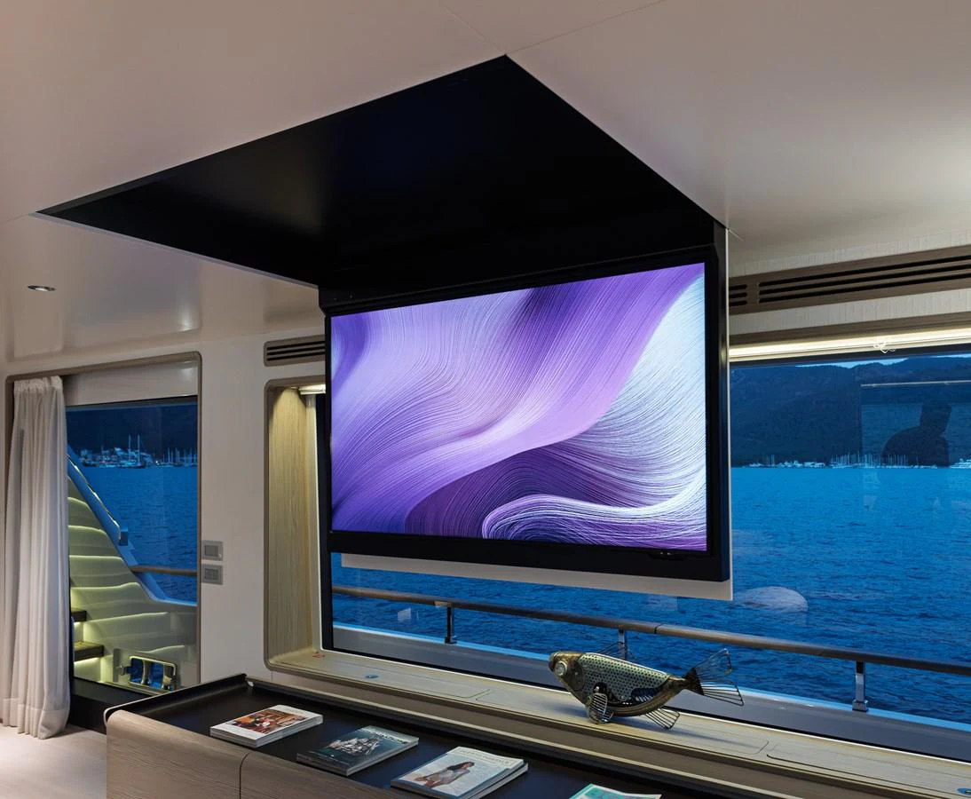 The yacht's interior features a modern entertainment area with a large TV and scenic views through the windows. aboard BELLE ILE Yacht for Sale