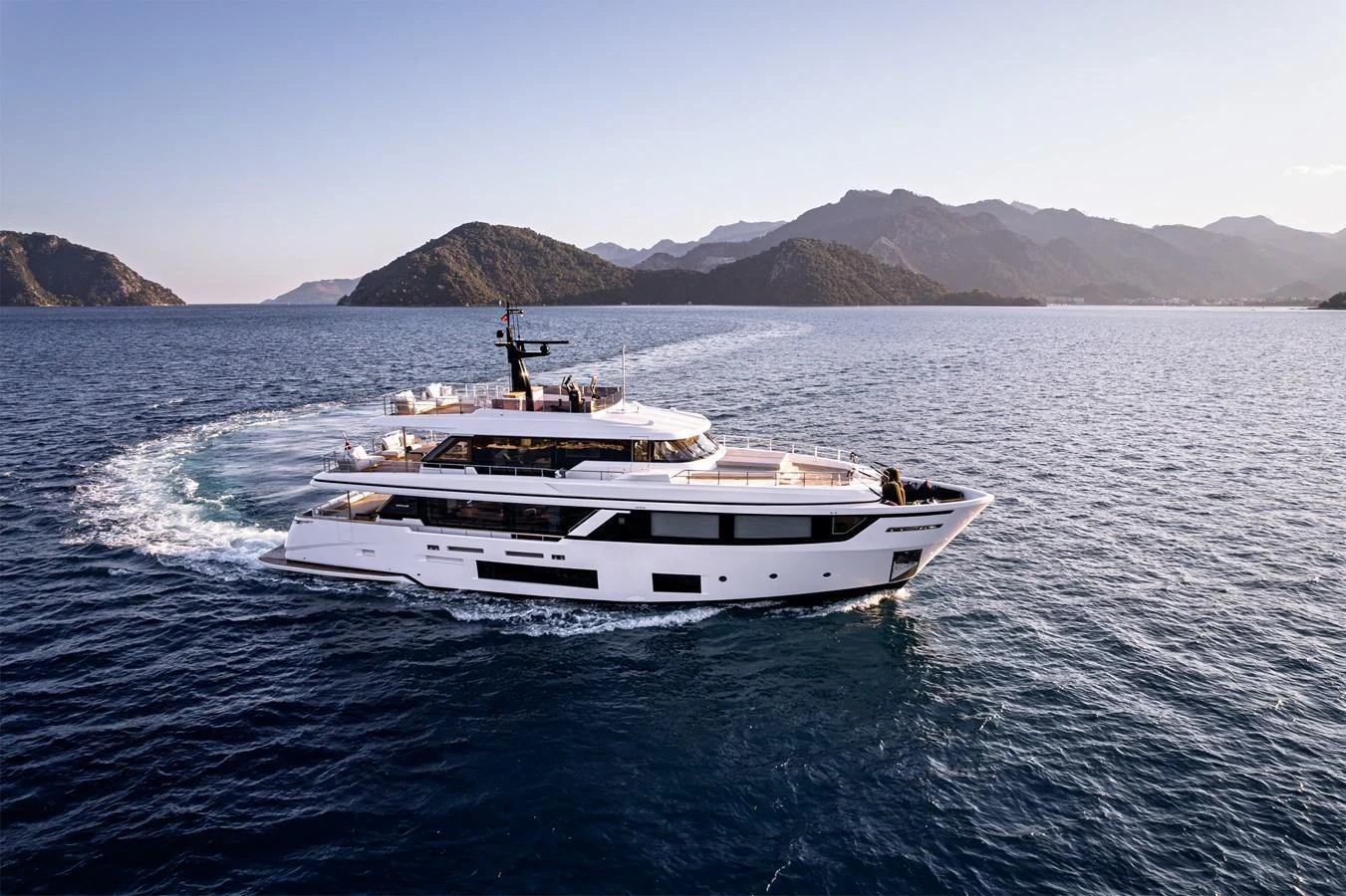 A sleek and modern yacht cruises through serene waters with a backdrop of picturesque mountains. aboard BELLE ILE Yacht for Sale