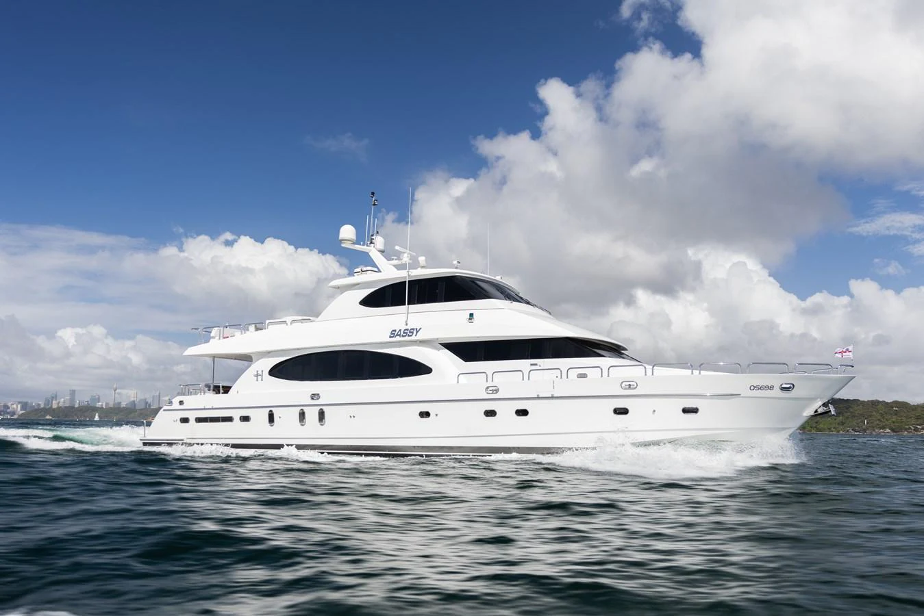 A sleek white yacht cruises through the water under a partly cloudy sky. aboard SASSY Yacht for Sale
