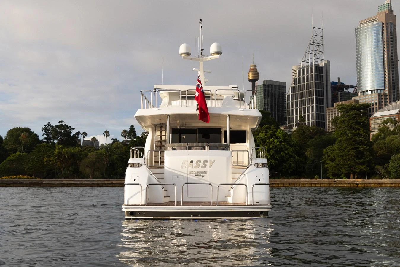 The yacht is seen from the rear, showcasing its elegant design and city backdrop. aboard SASSY Yacht for Sale