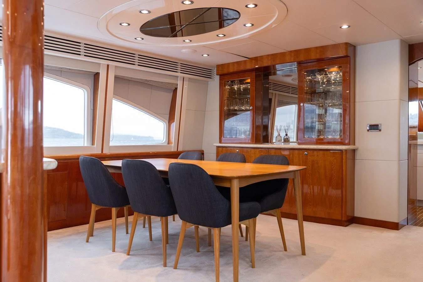 The yacht's dining area features a sleek wooden table surrounded by comfortable chairs, with large windows providing a scenic view. aboard SASSY Yacht for Sale