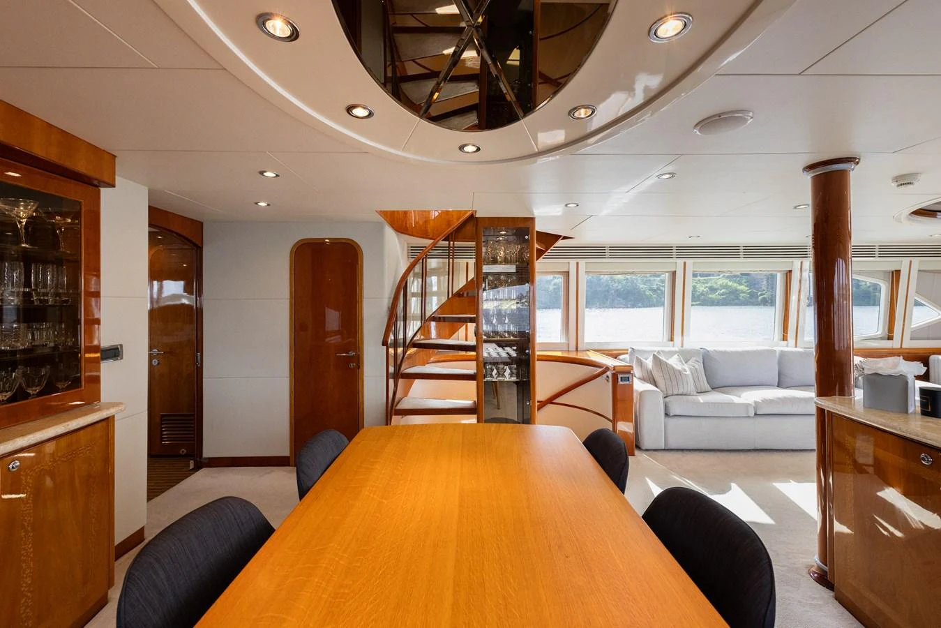 The yacht's dining area features a sleek wooden table, comfortable seating, and a spiral staircase leading to the upper deck. aboard SASSY Yacht for Sale