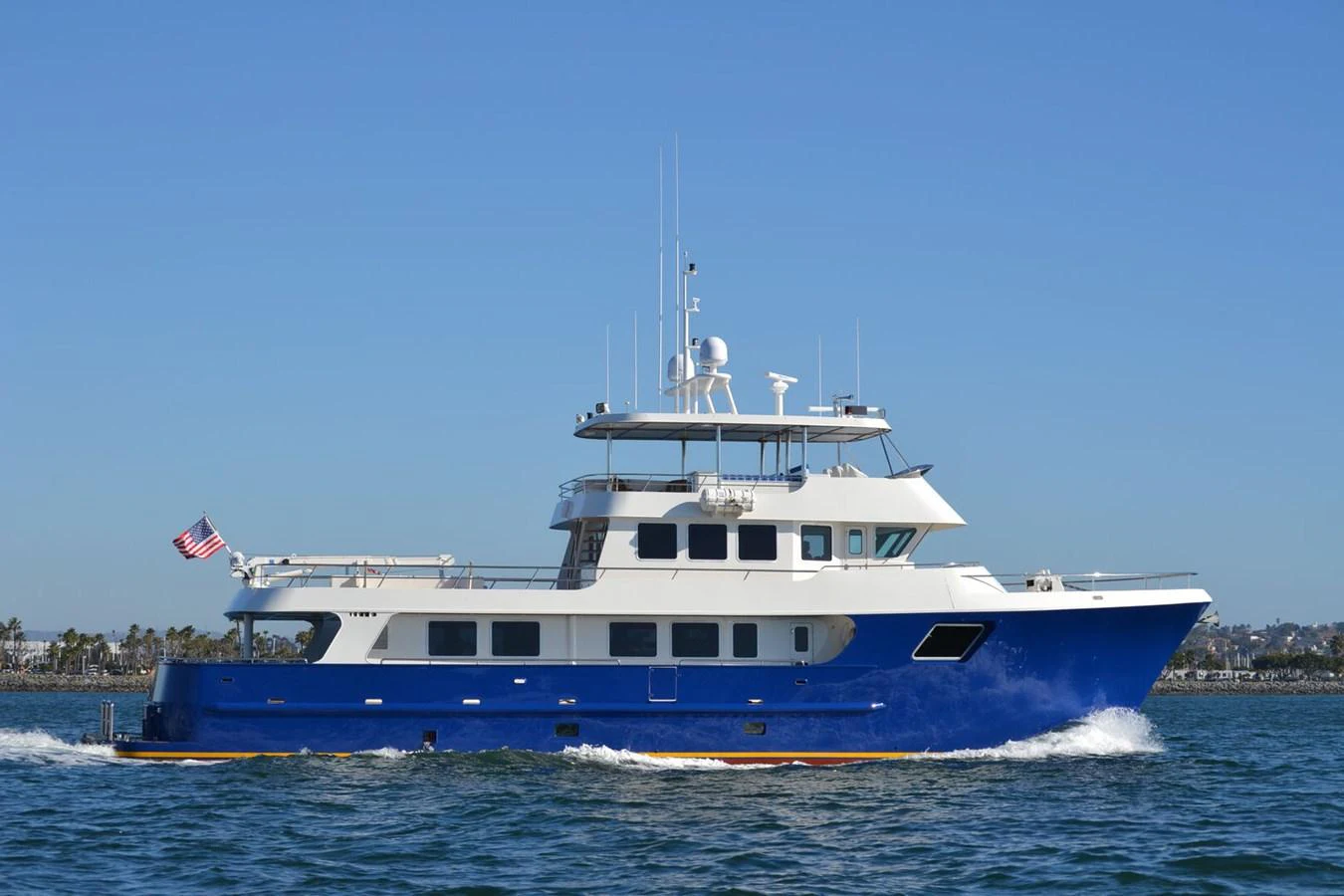 A striking blue and white yacht cruises smoothly on the water under a clear sky. aboard HEAVEN'S GATE Yacht for Sale