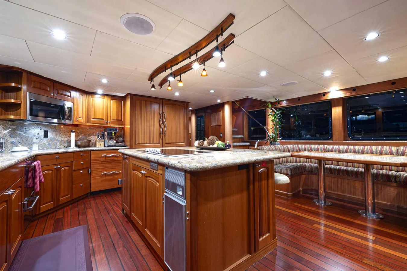 The yacht's galley features rich wooden cabinetry, modern appliances, and a spacious dining area with plush seating. aboard HEAVEN'S GATE Yacht for Sale