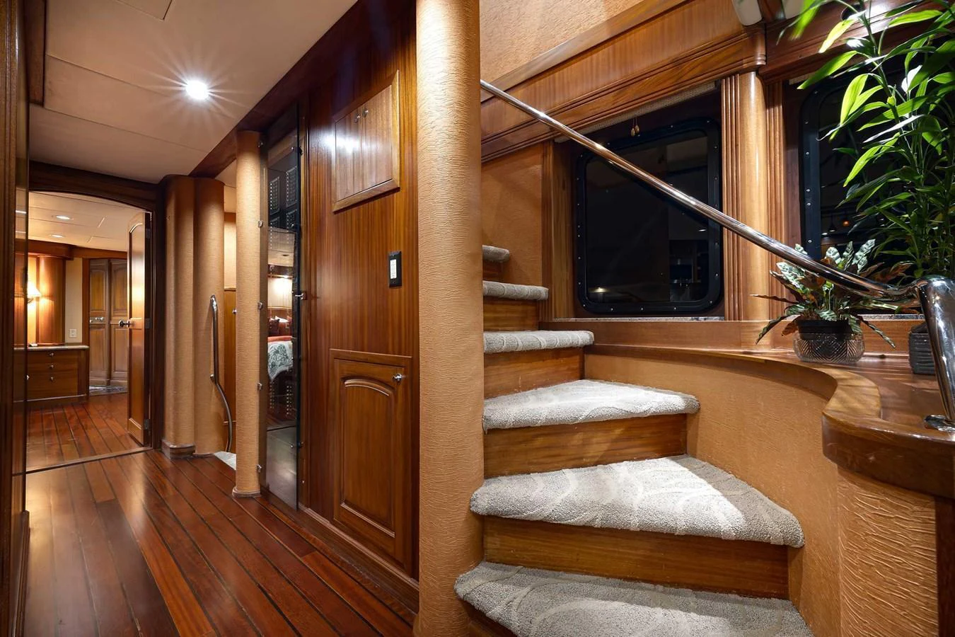 The yacht's interior features a beautifully crafted wooden staircase with elegant lighting and plush carpeting. aboard HEAVEN'S GATE Yacht for Sale