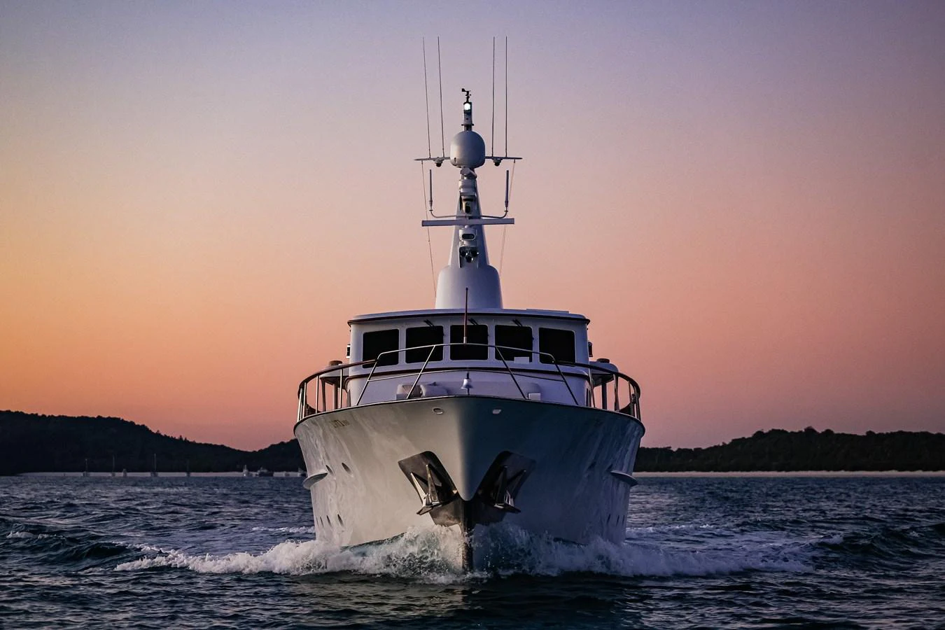 A sleek yacht is captured head-on, cruising through calm waters at sunset. aboard VICTORIA Yacht for Sale