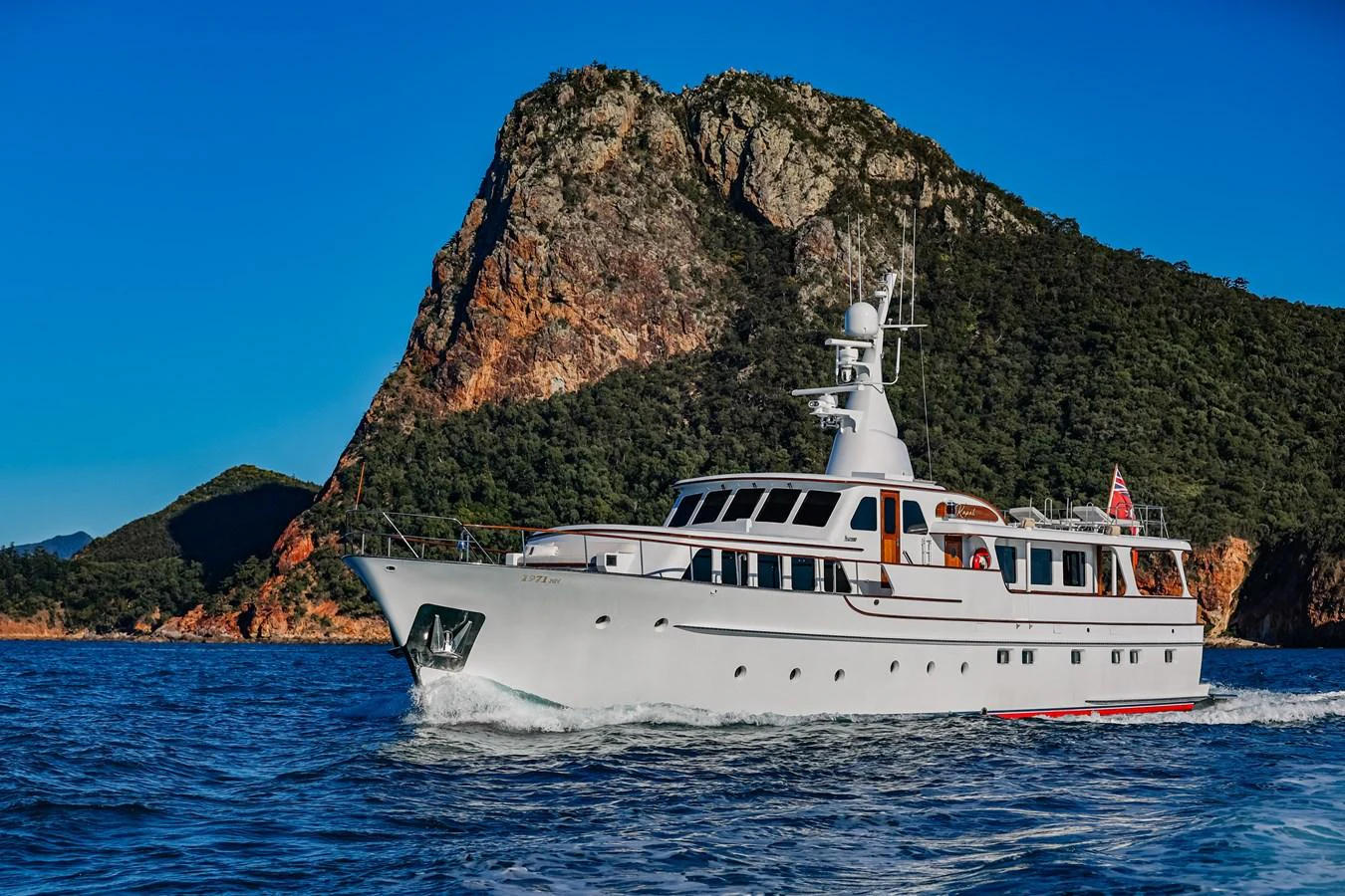 A classic yacht cruises gracefully against a stunning coastal backdrop. aboard VICTORIA Yacht for Sale