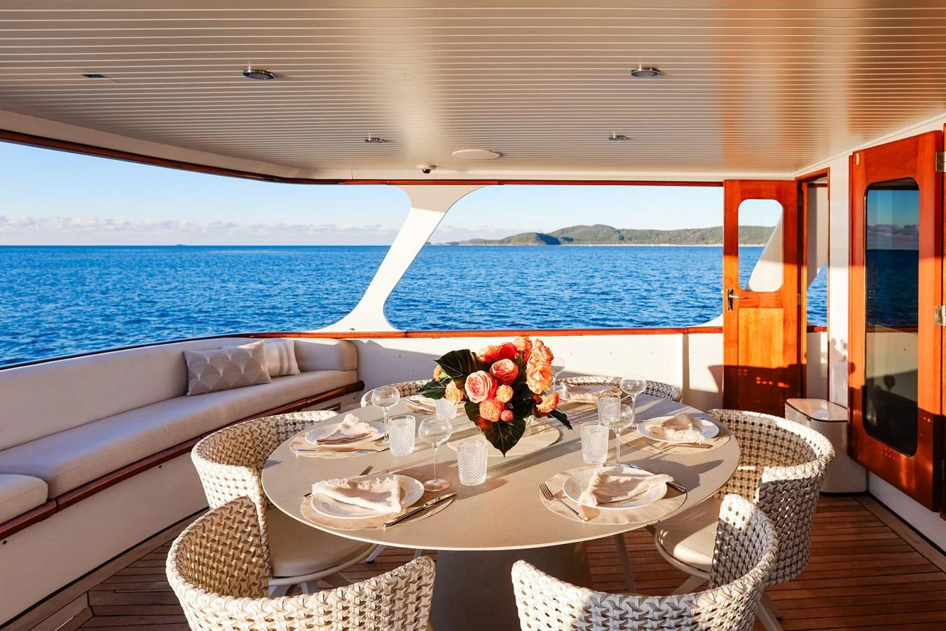 The aft deck features a stylish dining area with a round table and wicker chairs, offering stunning ocean views. aboard VICTORIA Yacht for Sale
