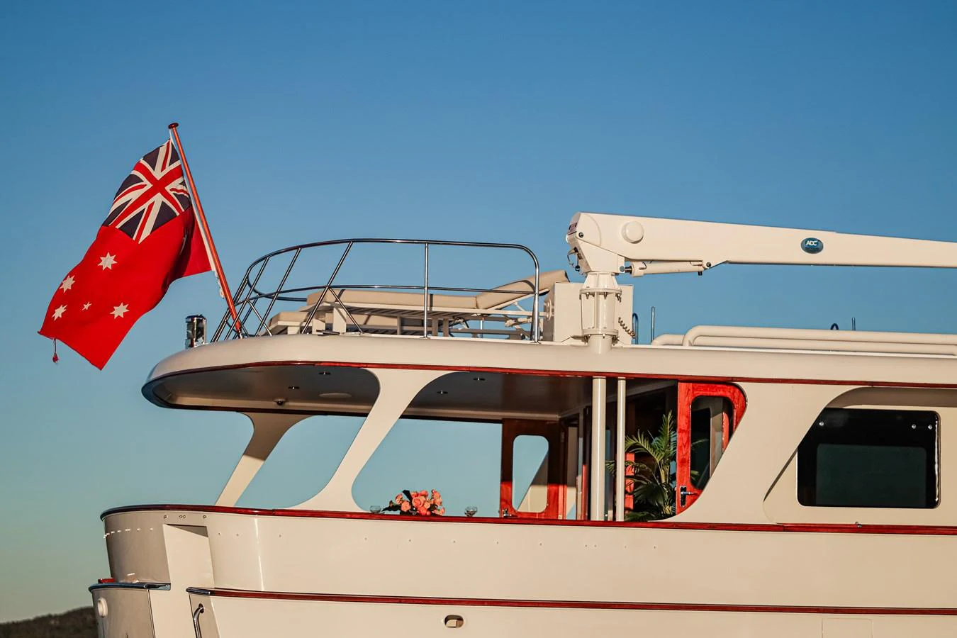 A classic yacht exterior with a prominent flag and clean lines under a clear sky. aboard VICTORIA Yacht for Sale