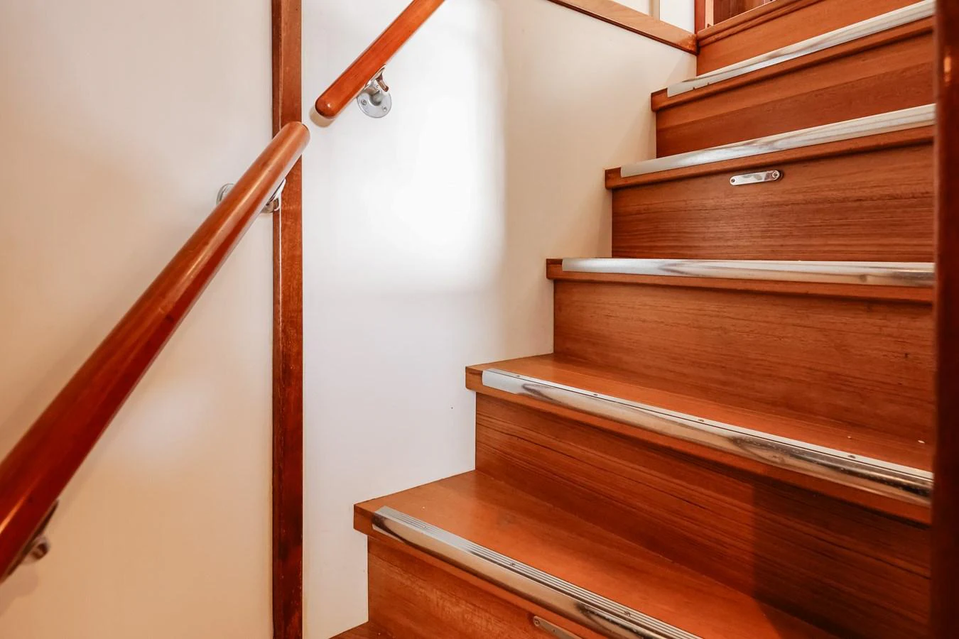 A polished wooden staircase with sleek metal accents leads to the upper deck. aboard VICTORIA Yacht for Sale