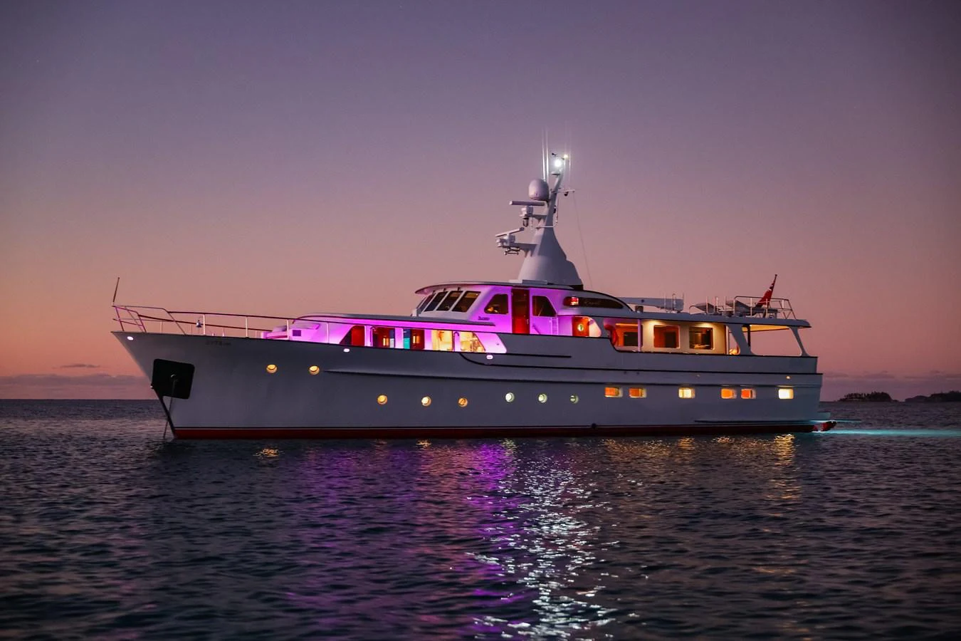 A luxurious yacht is beautifully illuminated against a serene twilight backdrop on calm waters. aboard VICTORIA Yacht for Sale