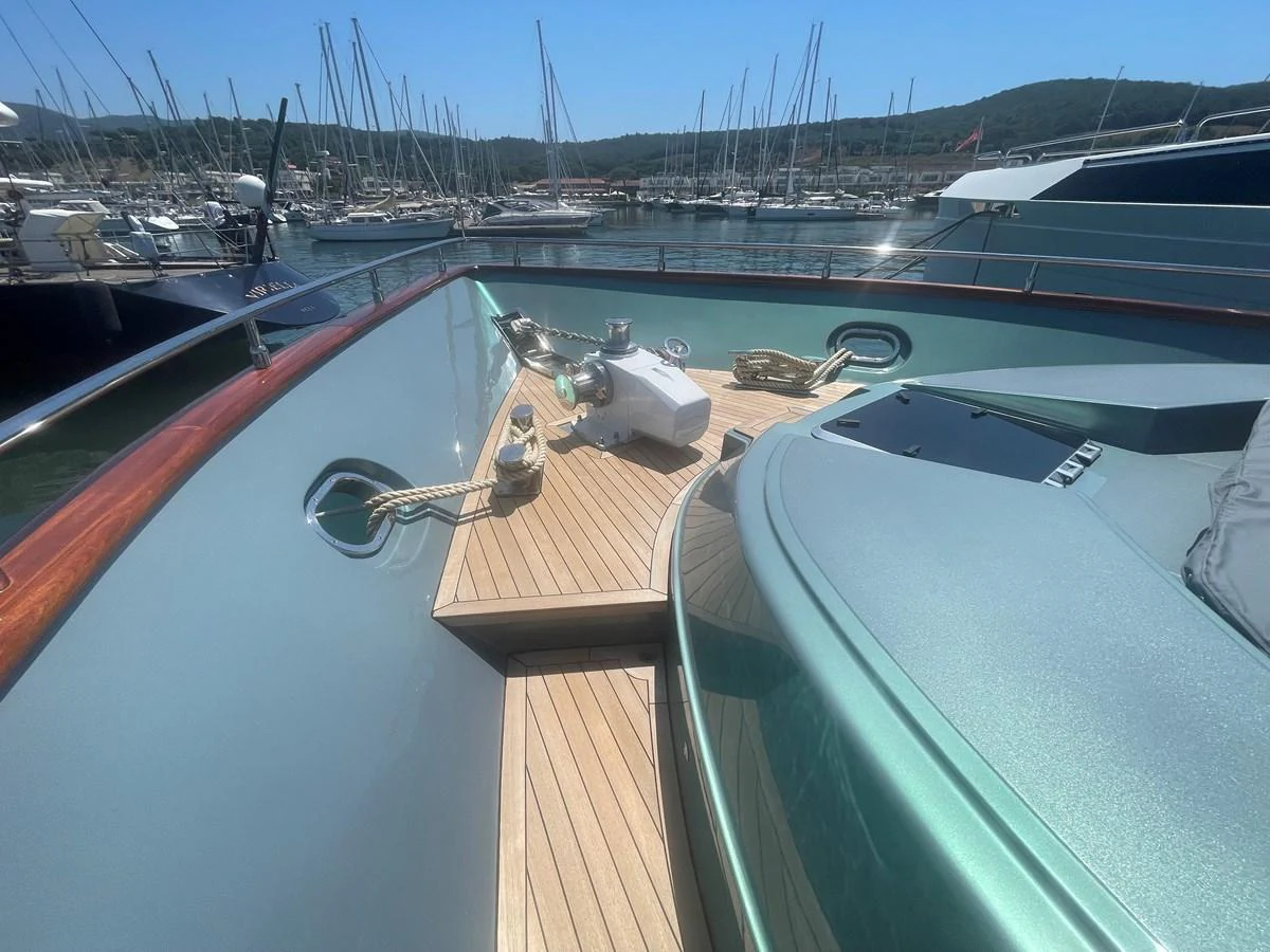 The foredeck showcases a sleek design with polished wood and metal accents, set against a marina backdrop. aboard UNICA Yacht for Sale