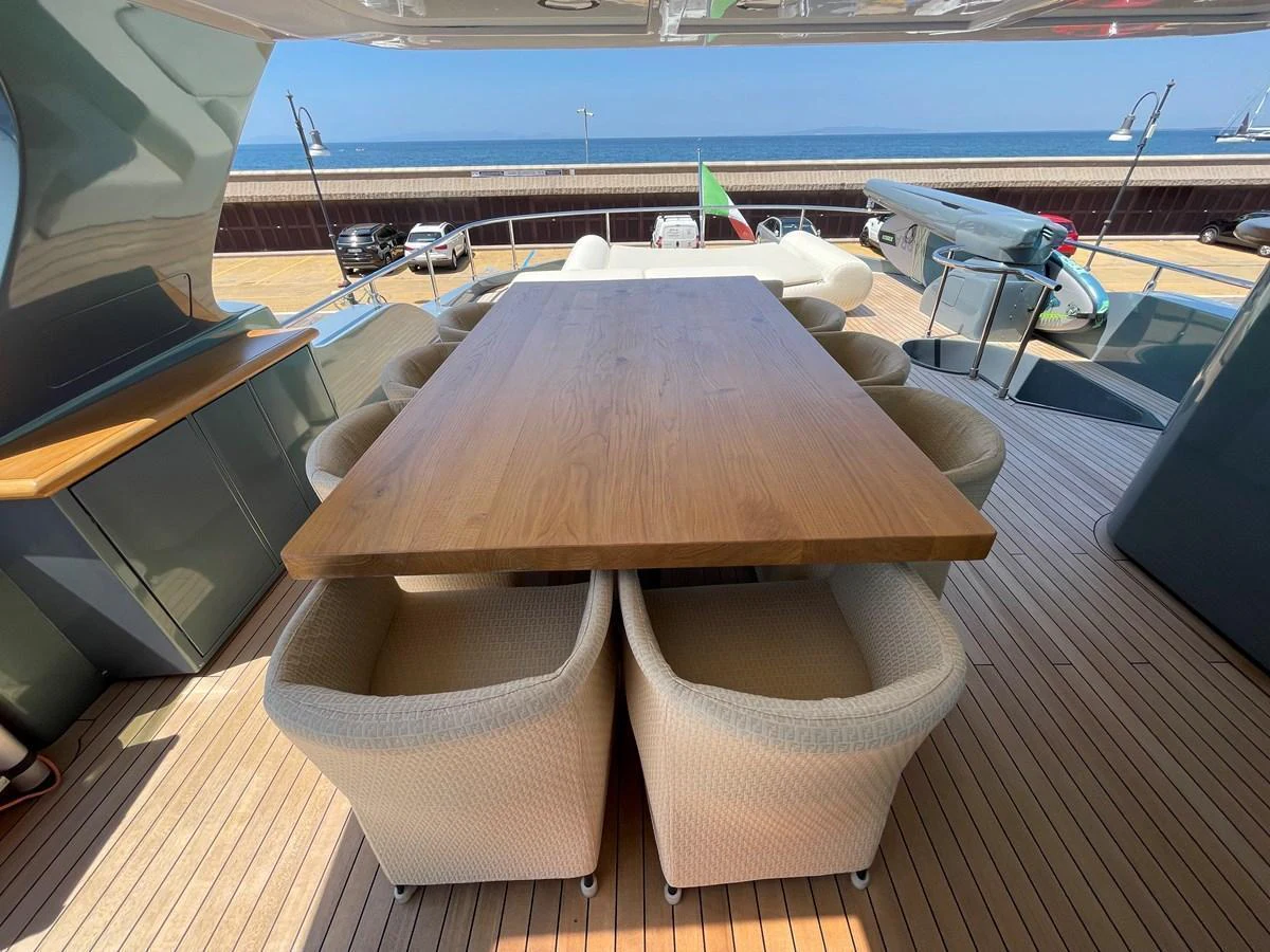 The aft deck features a spacious dining area with a large wooden table and comfortable chairs, perfect for alfresco meals with a view of the sea. aboard UNICA Yacht for Sale