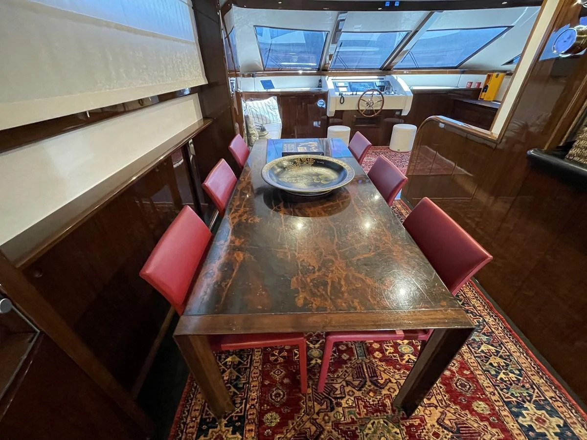 The yacht's dining area features a luxurious wooden table with red chairs, set against a backdrop of rich wood paneling and large windows. aboard UNICA Yacht for Sale
