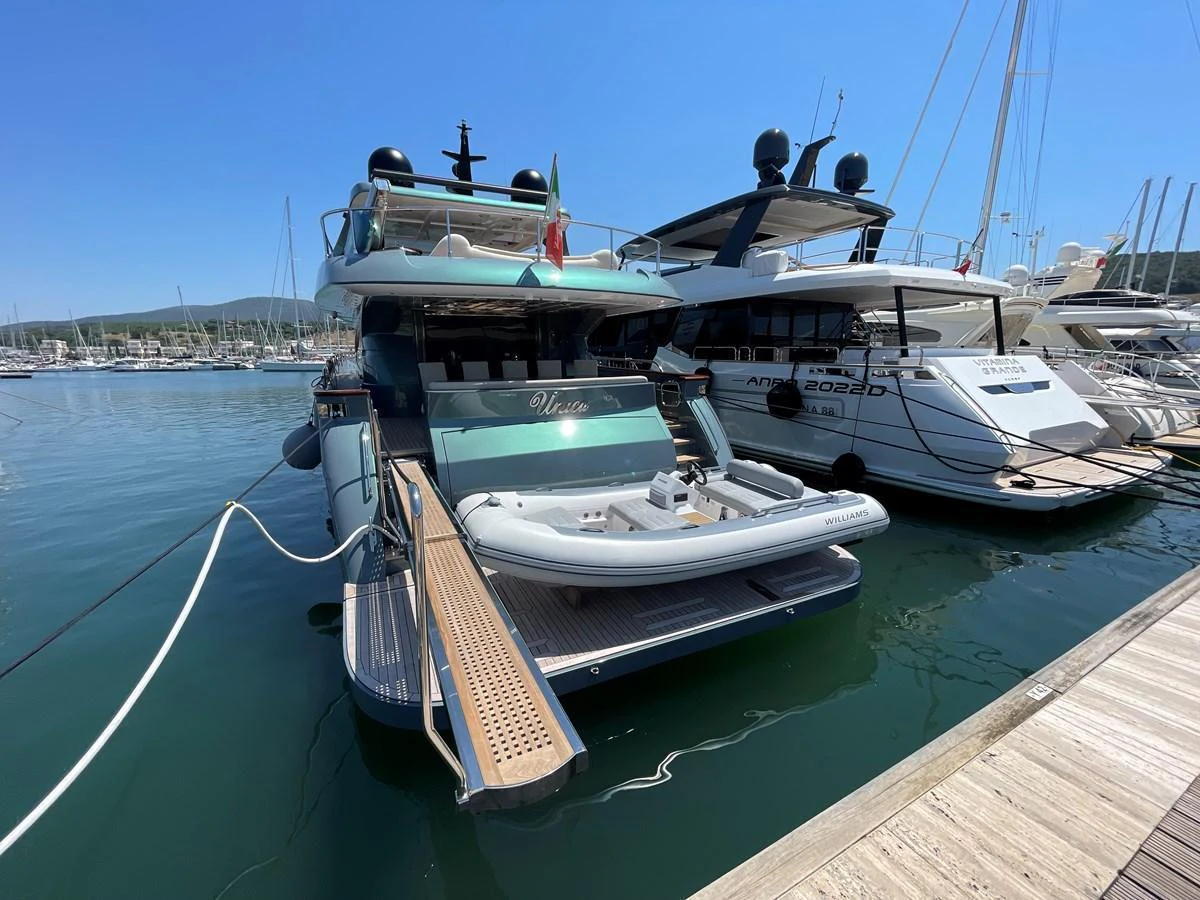 The yacht is docked at a marina, showcasing its aft deck with a tender boat on a hydraulic platform. aboard UNICA Yacht for Sale