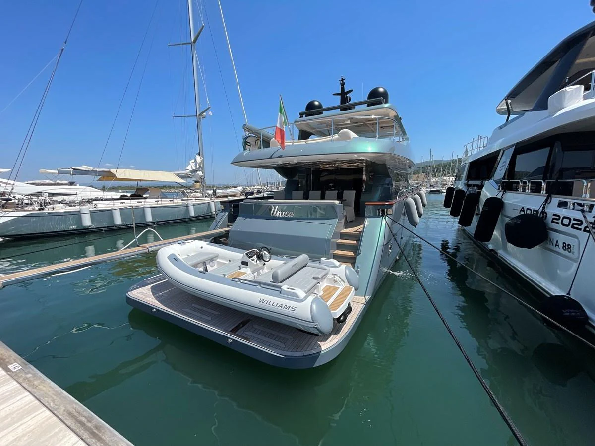 The yacht is docked at a marina, showcasing its spacious aft deck and tender. aboard UNICA Yacht for Sale