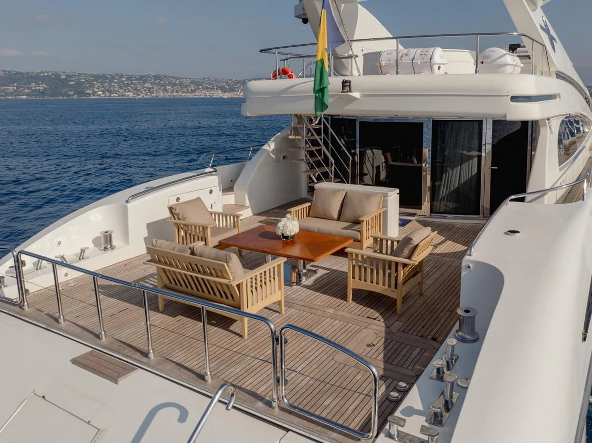 The aft deck features a stylish outdoor seating area with comfortable wooden furniture and a central table, perfect for relaxation and socializing. aboard M.J. TAKNM Yacht for Sale