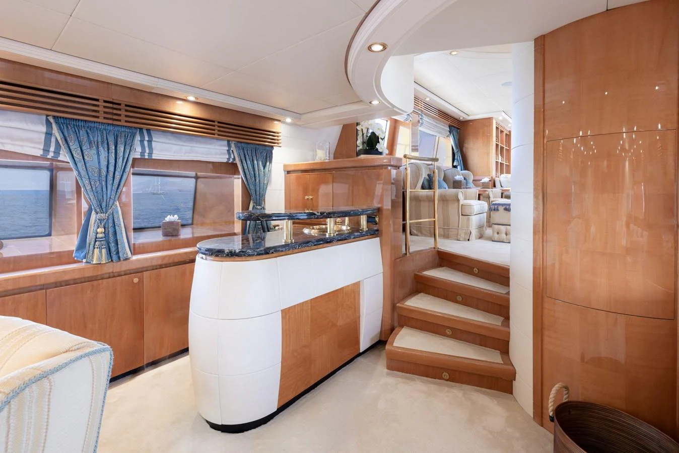 The yacht's salon features elegant wood paneling, plush seating, and large windows with ocean views. aboard M.J. TAKNM Yacht for Sale