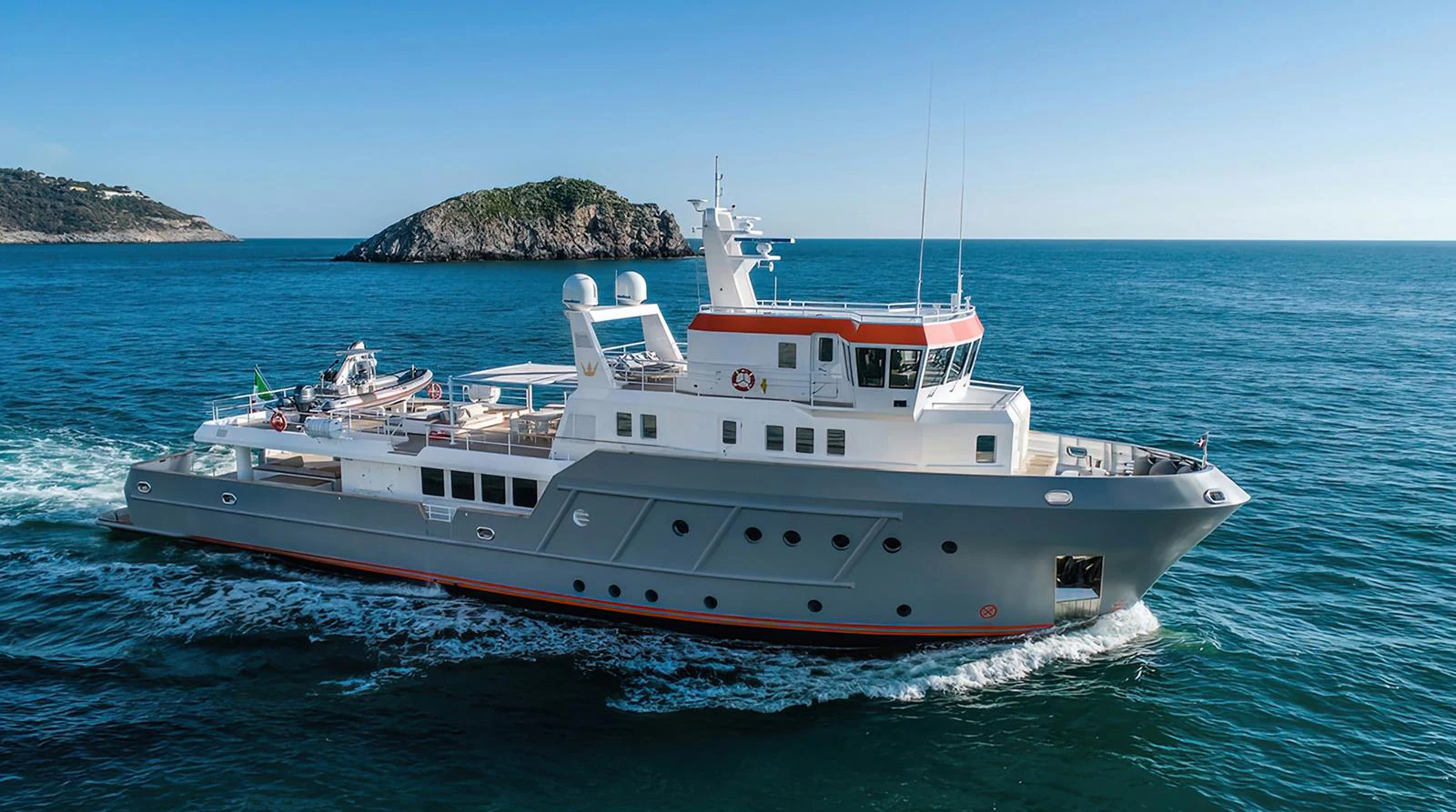 A robust and stylish yacht cruises through clear blue waters with a scenic island in the background. aboard EXPLORER 130 Yacht for Sale