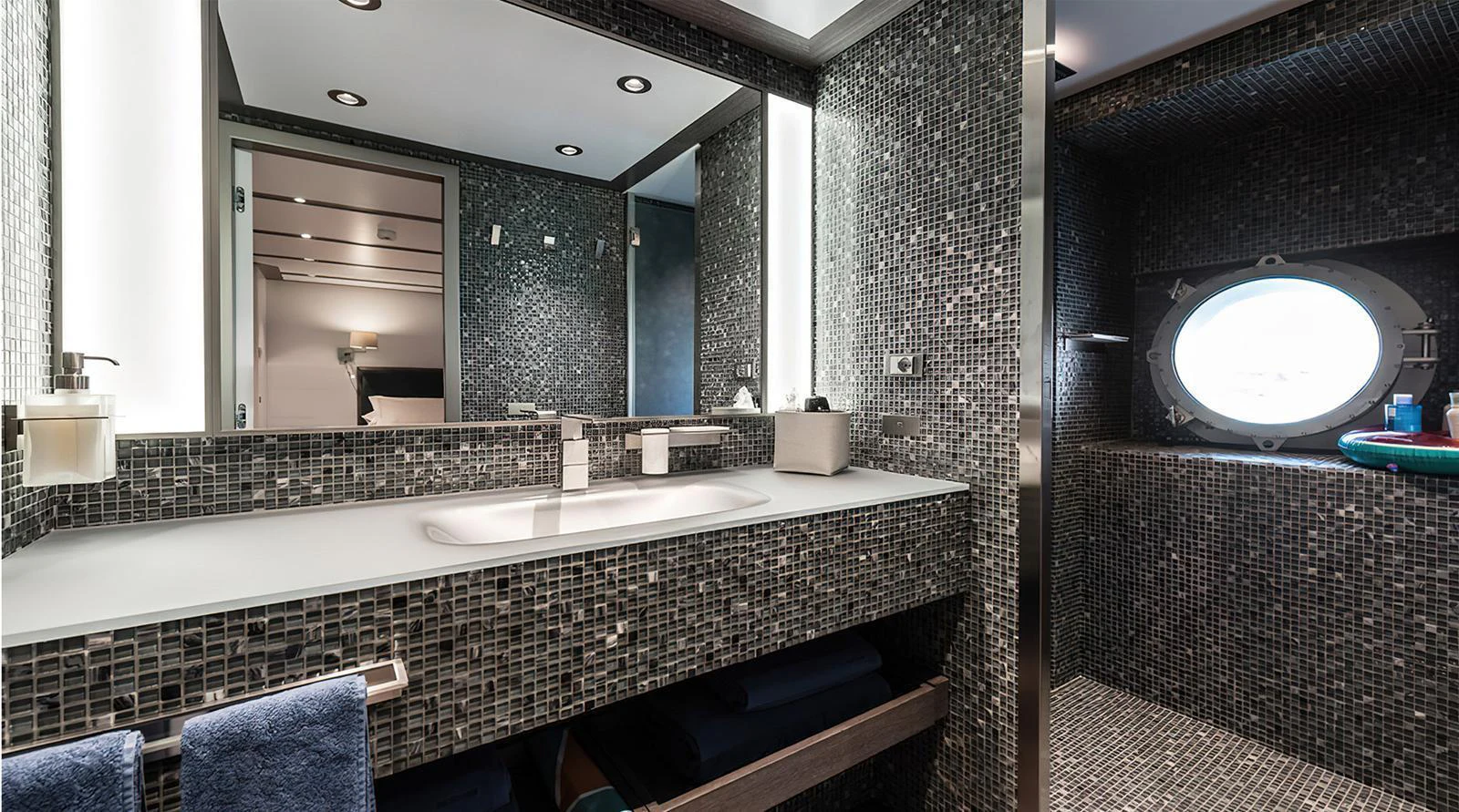 A modern yacht bathroom with mosaic tile walls and a round porthole window. aboard EXPLORER 130 Yacht for Sale