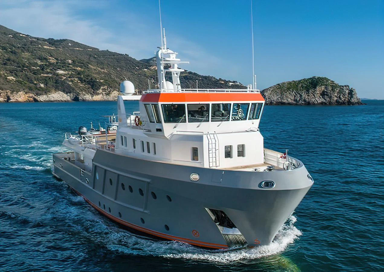A robust and stylish yacht cruising through clear blue waters with scenic coastal views in the background. aboard EXPLORER 130 Yacht for Sale