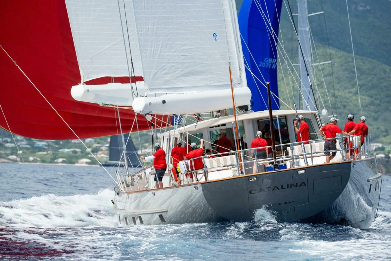 A sleek sailing yacht with vibrant sails glides through the water, crewed by a team in matching red shirts. aboard CATALINA Yacht for Sale