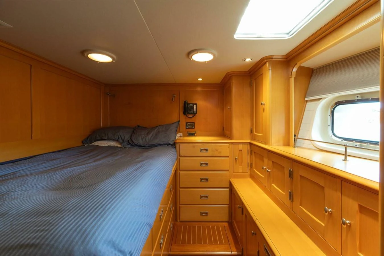 A cozy cabin with wooden cabinetry and a comfortable bed, illuminated by natural light from a porthole. aboard CATALINA Yacht for Sale