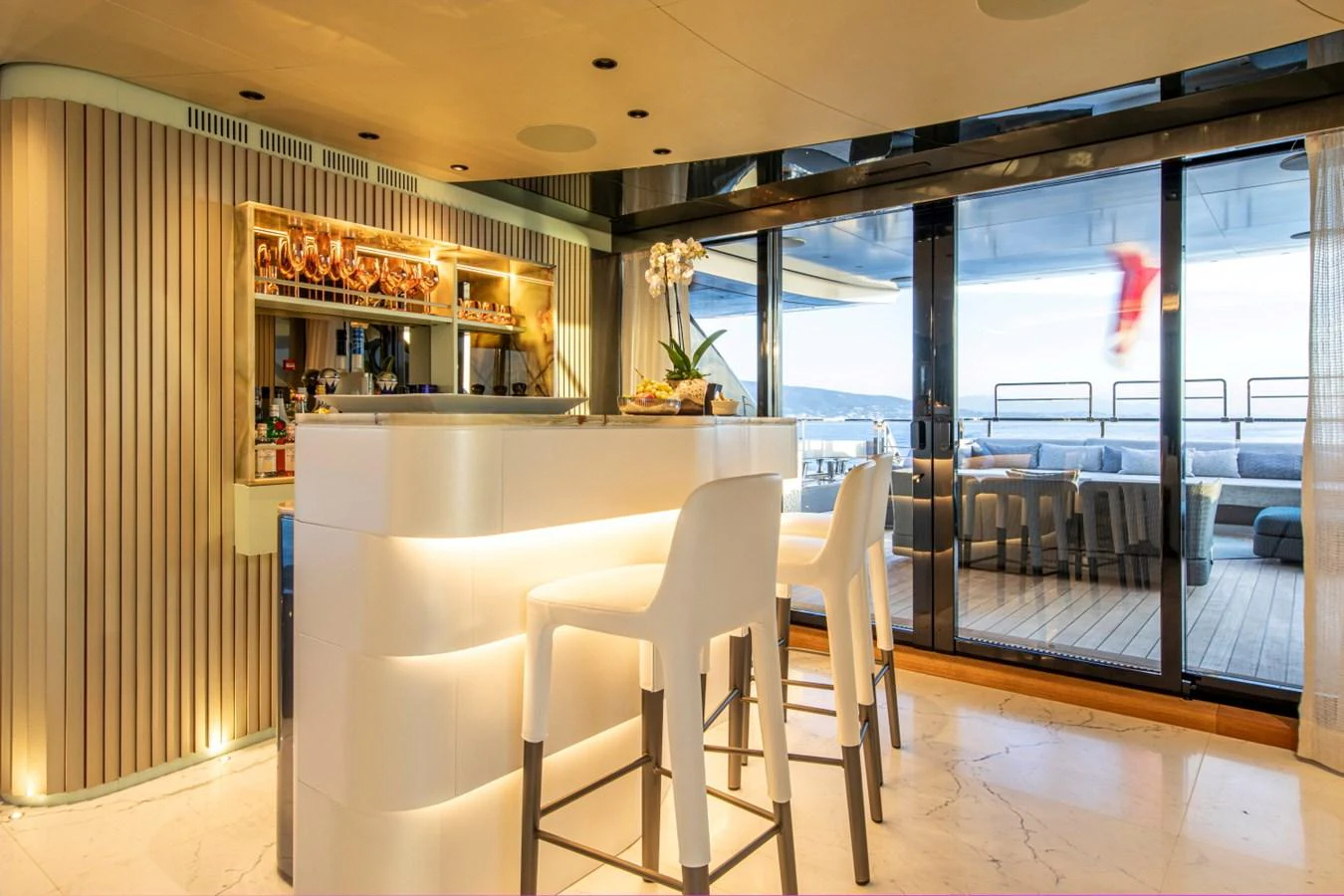 The yacht's interior features a stylish bar area with modern seating and a view of the deck through large glass doors. aboard PACIFIC PEARL Yacht for Sale