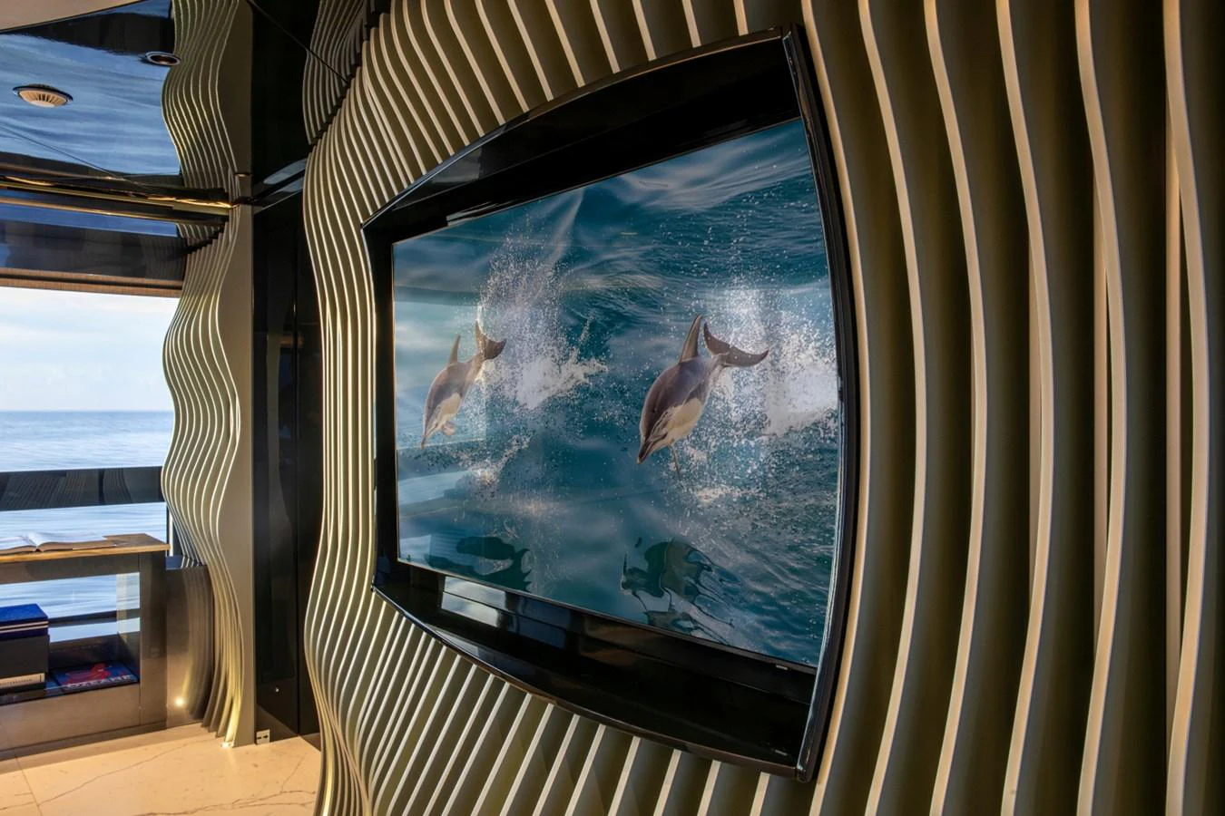 The yacht's interior features a stylish entertainment area with a large screen displaying dolphins. aboard PACIFIC PEARL Yacht for Sale
