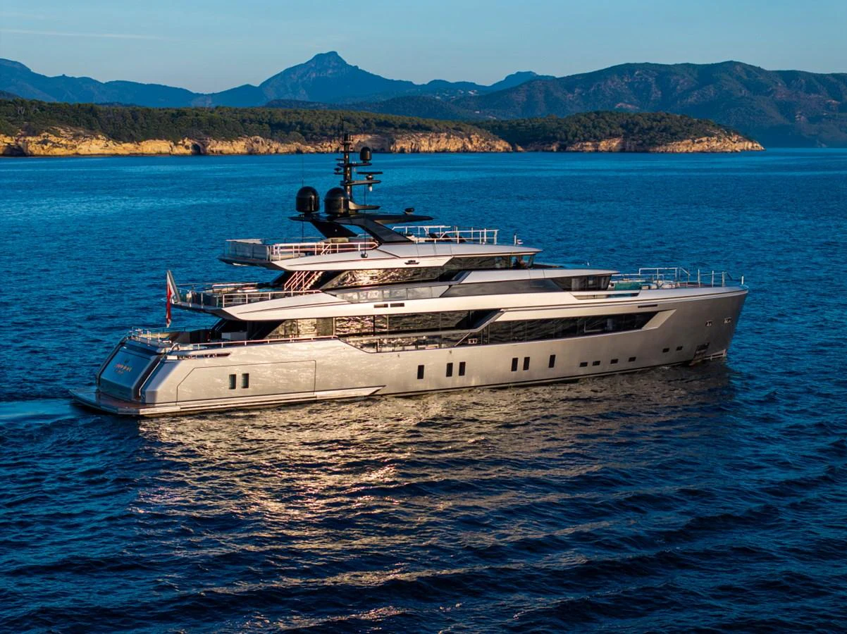 A sleek and modern yacht cruises through serene blue waters with a picturesque mountainous backdrop. aboard PACIFIC PEARL Yacht for Sale