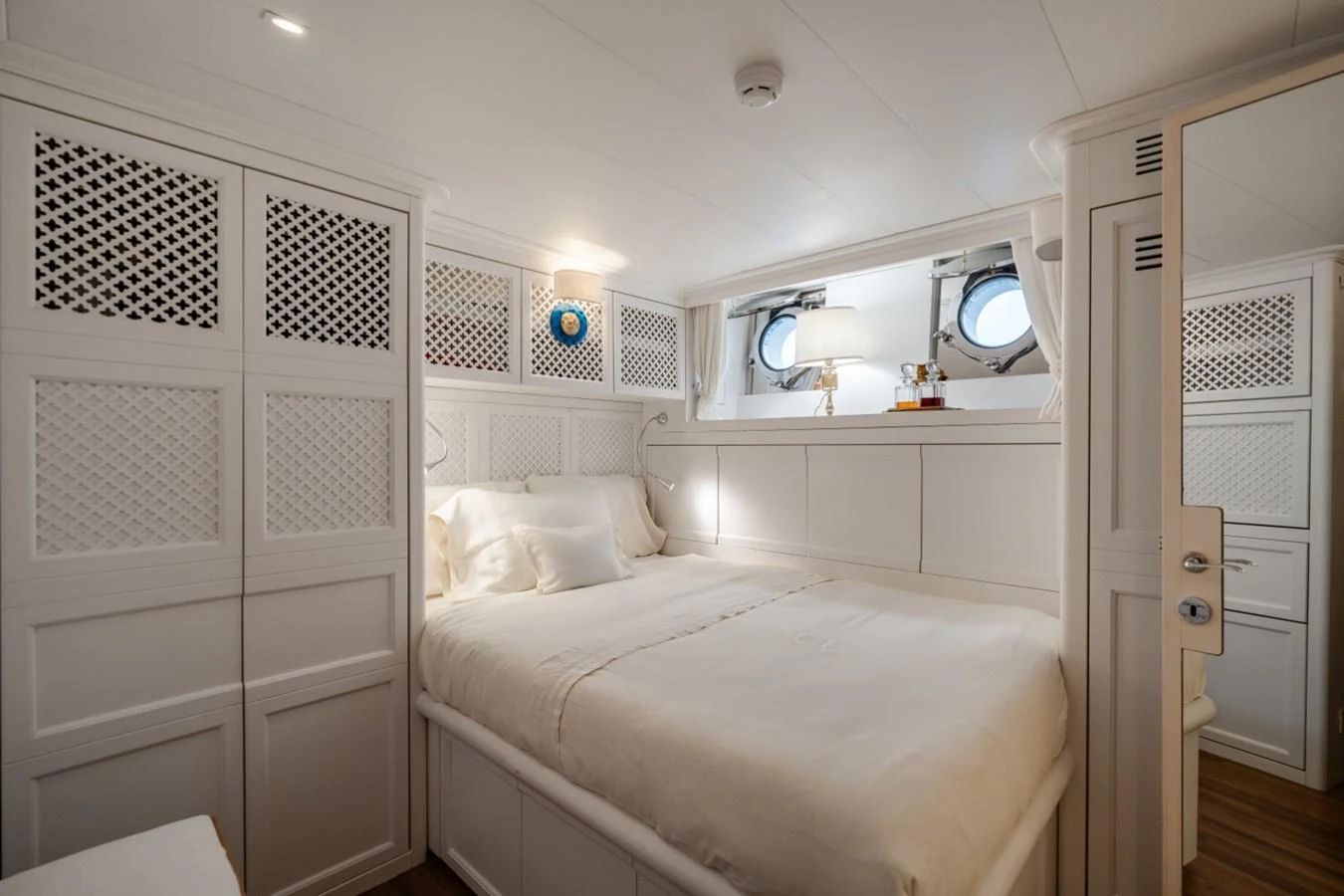 The stateroom features a cozy bed with elegant white furnishings and natural light from portholes. aboard DIONE STAR Yacht for Sale