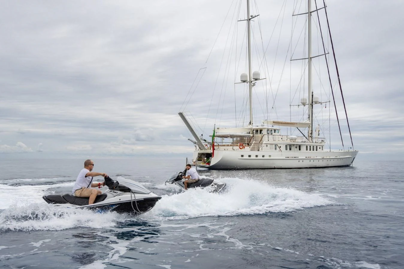 A luxurious yacht is anchored on calm waters while two people enjoy jet skiing nearby. aboard DIONE STAR Yacht for Sale