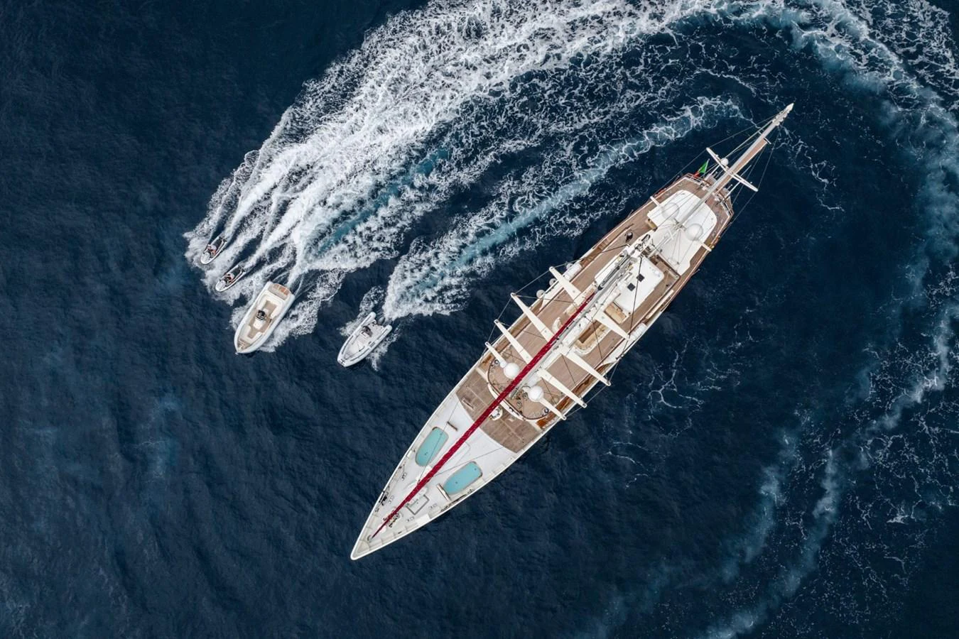 A stunning aerial view of a luxurious yacht cruising through the water, accompanied by smaller boats. aboard DIONE STAR Yacht for Sale