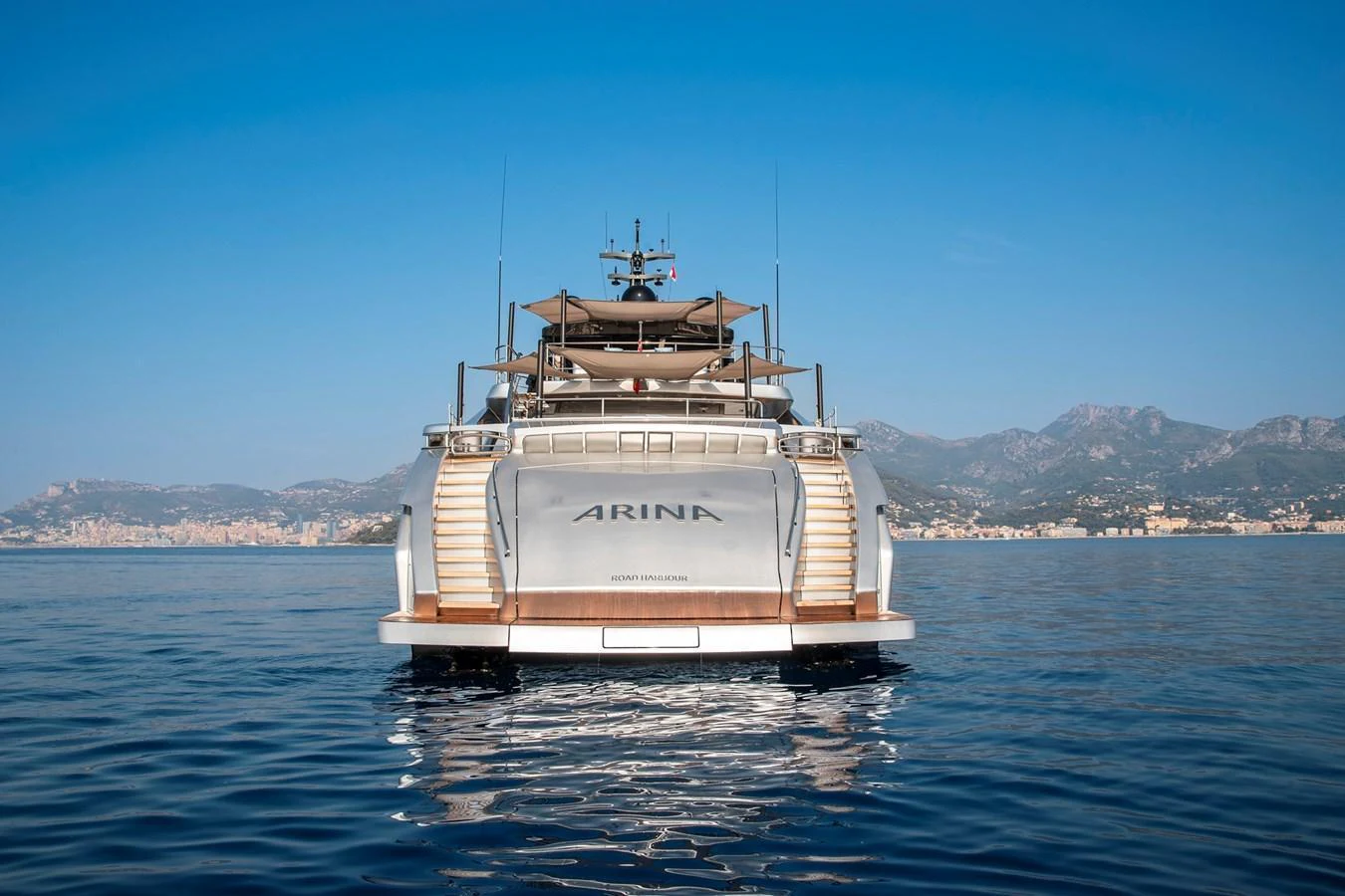 The yacht is seen from the stern, showcasing its sleek design and luxurious features against a serene coastal backdrop. aboard PERSHING 140 Yacht for Sale