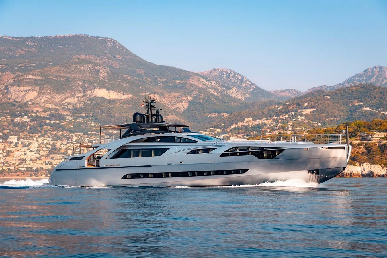A sleek and modern yacht cruising along a picturesque coastline with mountains in the background. aboard PERSHING 140 Yacht for Sale