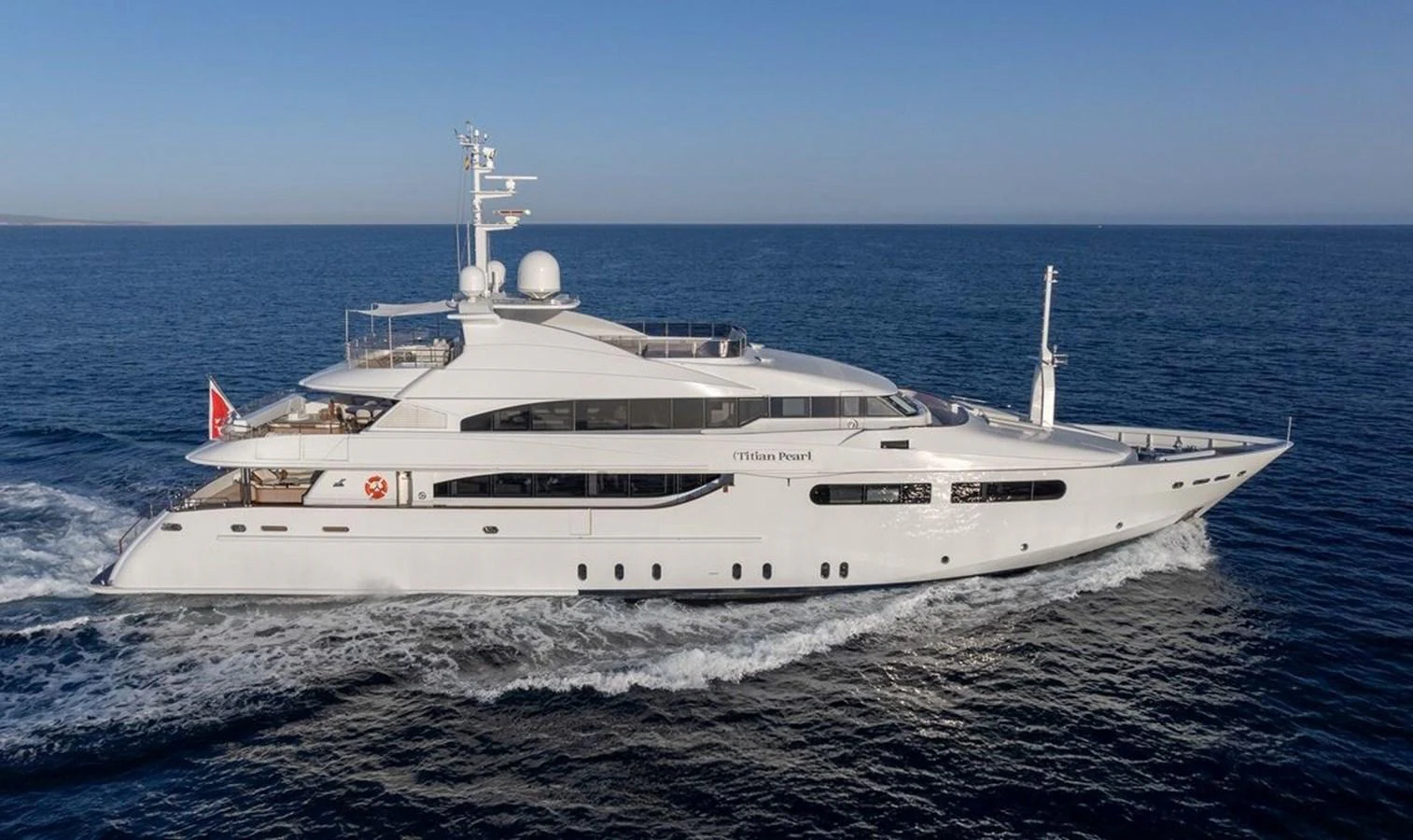 A sleek and modern yacht cruising on calm blue waters under a clear sky. aboard TITIAN PEARL Yacht for Sale