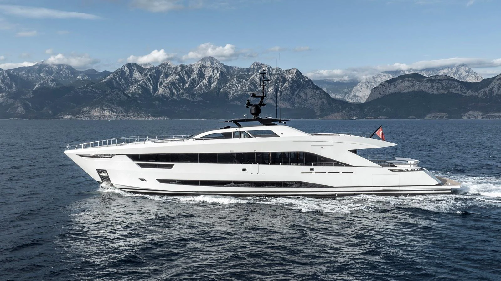 A sleek and modern yacht cruising on calm waters with a mountainous backdrop. aboard XIMENA Yacht for Sale