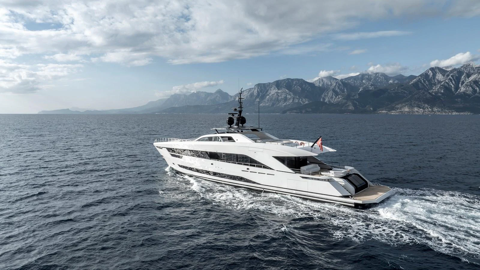 A sleek and modern yacht cruises through open waters with a stunning mountainous backdrop. aboard XIMENA Yacht for Sale