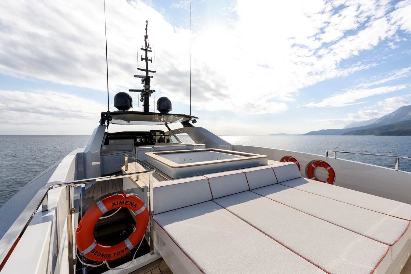 The yacht's sundeck features a spacious sunbathing area with plush cushions and a hot tub, set against a serene ocean backdrop. aboard XIMENA Yacht for Sale