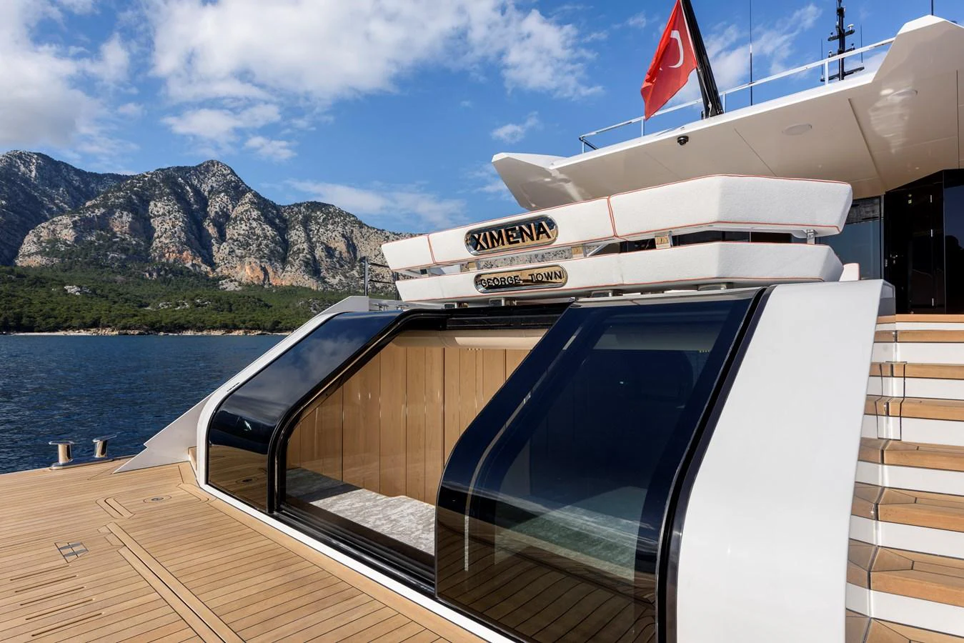 The yacht features a sleek, modern design with expansive glass doors and a spacious deck area. aboard XIMENA Yacht for Sale