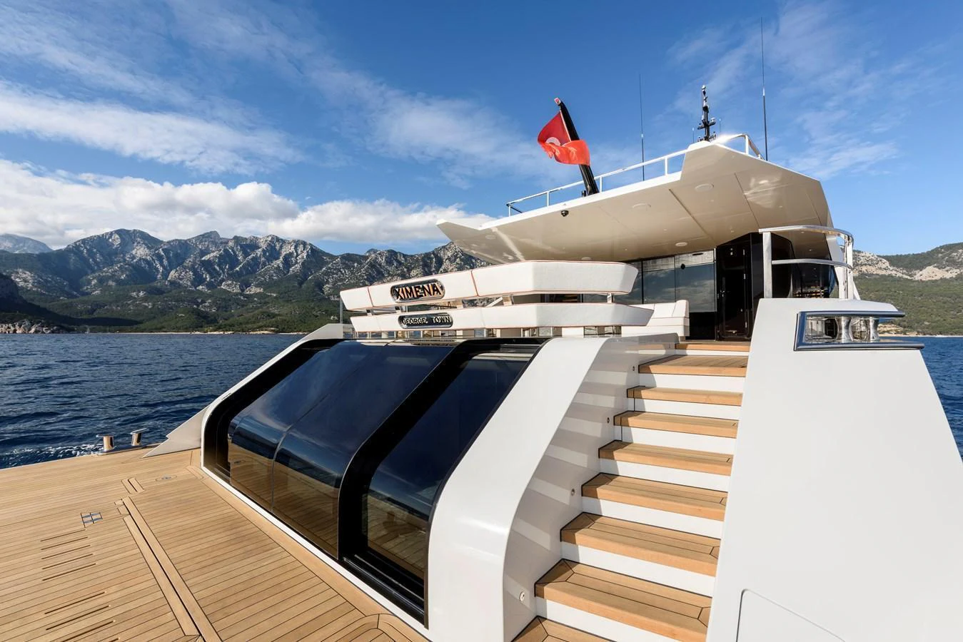 The yacht's aft deck showcases sleek design and luxurious finishes with a backdrop of stunning coastal scenery. aboard XIMENA Yacht for Sale