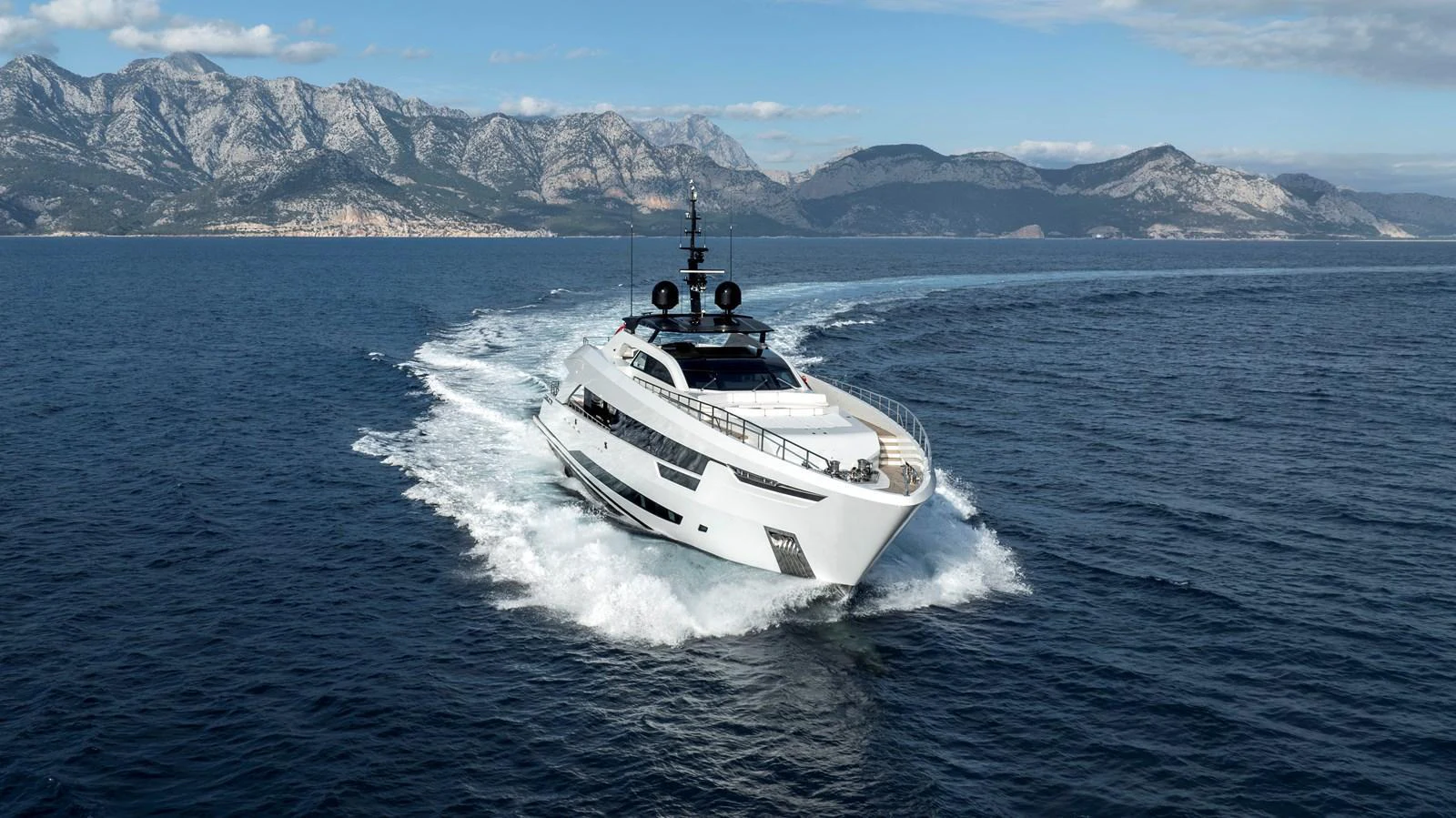 A sleek yacht cruises through the open sea with a stunning mountainous backdrop. aboard XIMENA Yacht for Sale