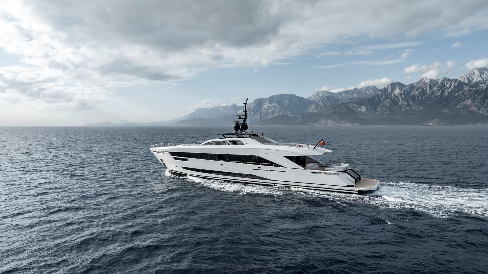 A sleek and modern yacht cruises through open waters with a mountainous backdrop. aboard XIMENA Yacht for Sale