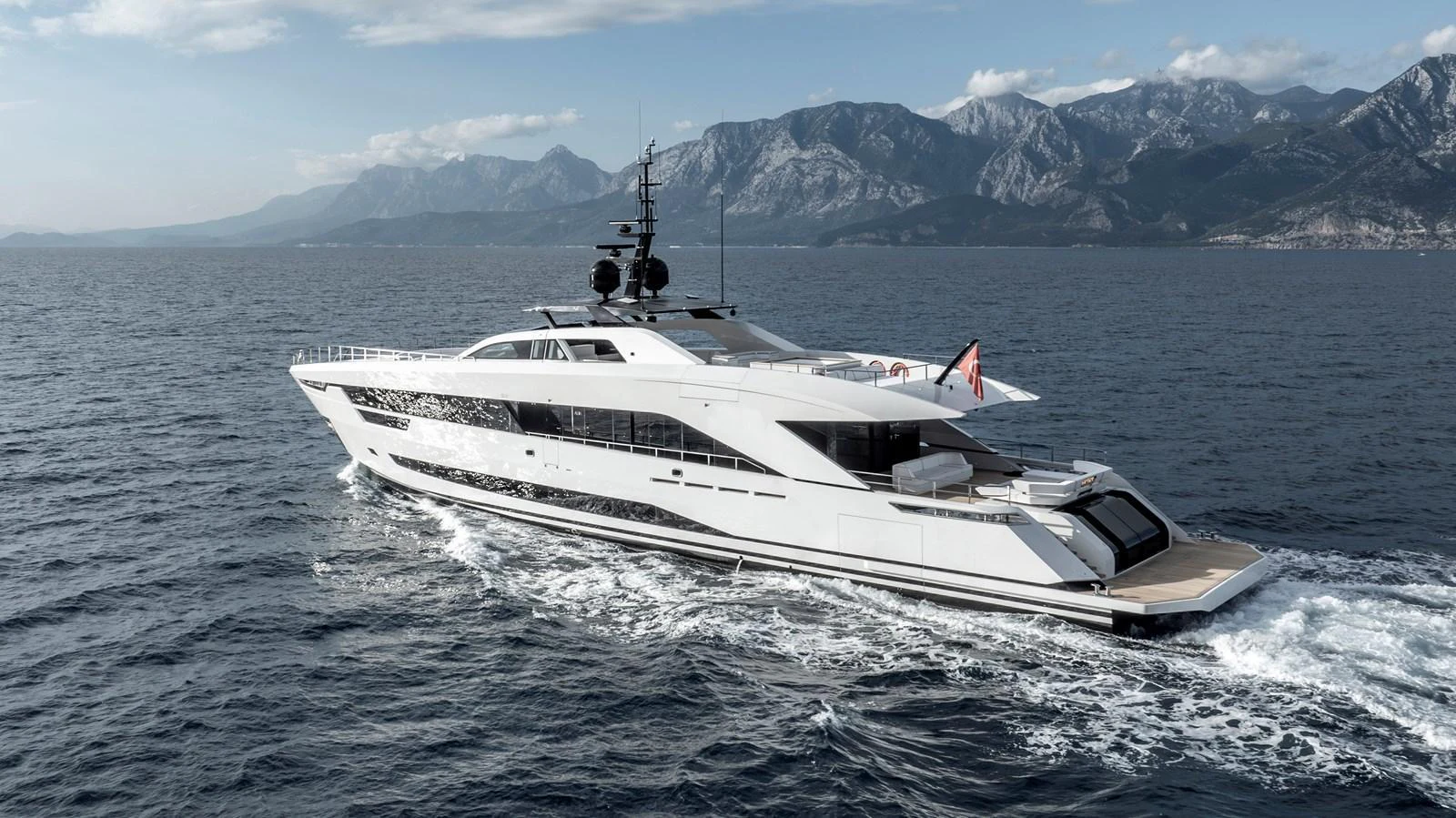 A sleek and modern yacht cruising on the open sea with a mountainous backdrop. aboard XIMENA Yacht for Sale